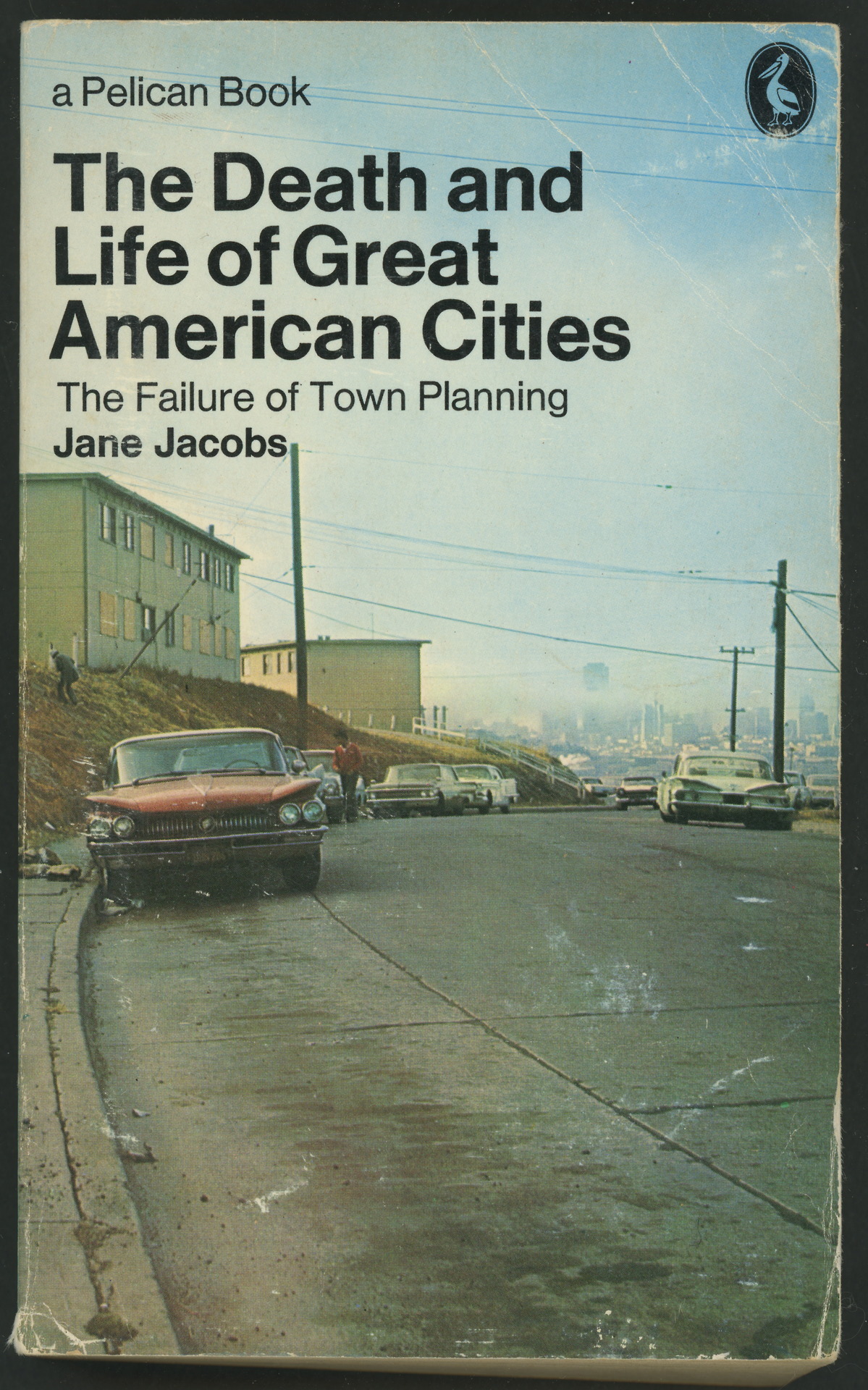 book cover with a vintage photo of a wide city street with a few cars parked and a couple buildings, superimposed with the title and author in Helvetica.